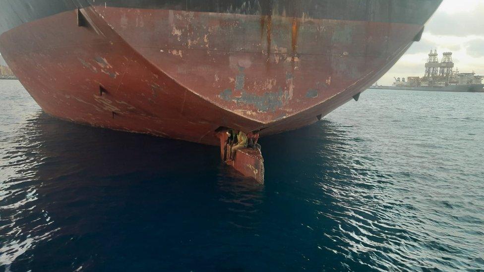 Three people sitting on a ship's rudder