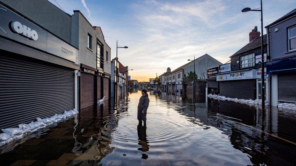 A man stands in the middle of a flooded street in Downpatrick