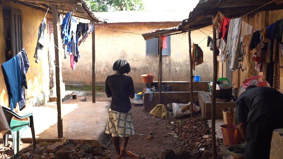 A young woman stands in a court yard with her back to us