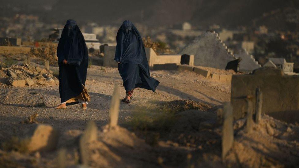 women in burqas walk along a dusty road at sunset