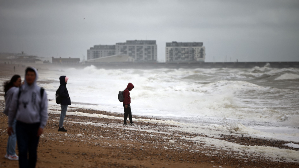 People on a beach with raincoats looking out to a rough sea