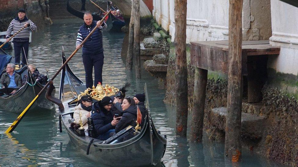 Gondolas a punted along a Venice canal showing visible signs of low water levels