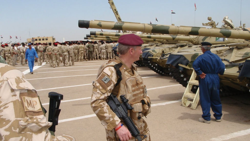 Many soldiers standing on the tarmac at an airbase with planes in the background