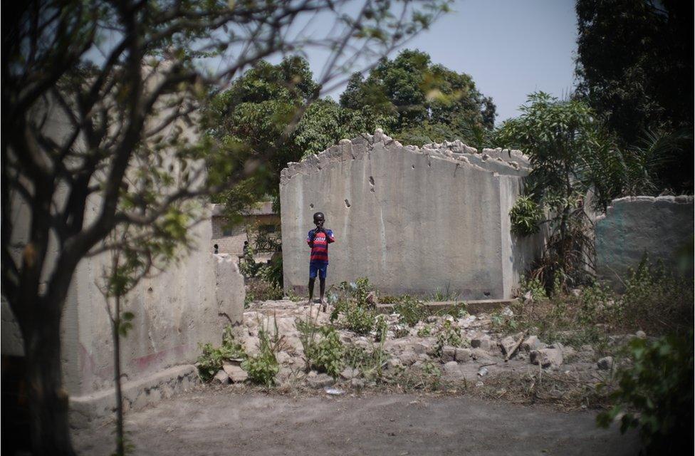 A boy stands alone in the ruins of a building