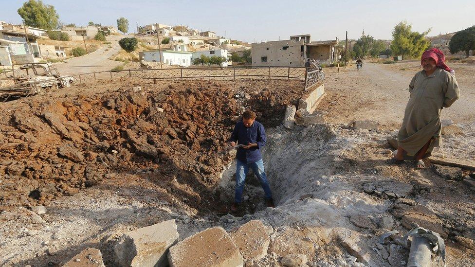 Men stand along a crater caused by what activists said was a Russian air strike in Latamneh city in the northern countryside of Hama