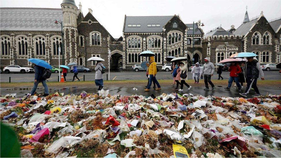 People walk past flowers and tributes displayed in memory of the twin mosque massacre victims outside the Botanical Gardens in Christchurch