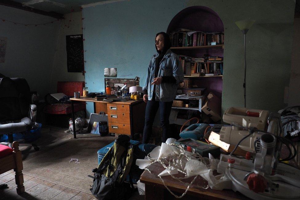 A woman standing alone in a room surrounded by furniture and tools