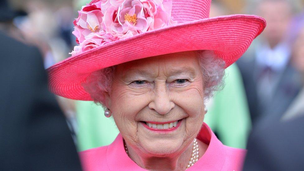 Photo of the Queen smiling and wearing a bright pink hat