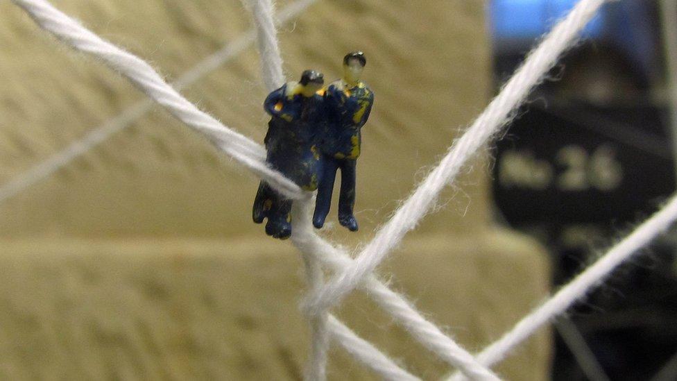 Tiny figures in a web of fabric