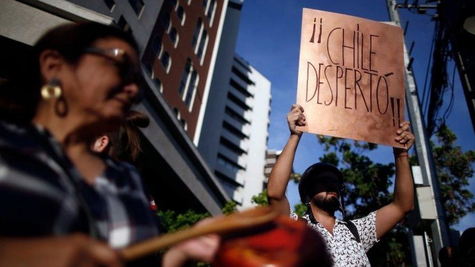 A demonstrator bangs a pot as another holds a sign reading "Chile has woken up" as they demonstrate in Santiago on 21 October, 2019.