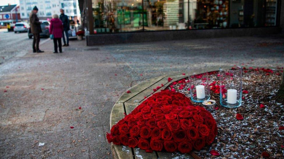 Flowers in the shape of a heart, with some candles on a bench.