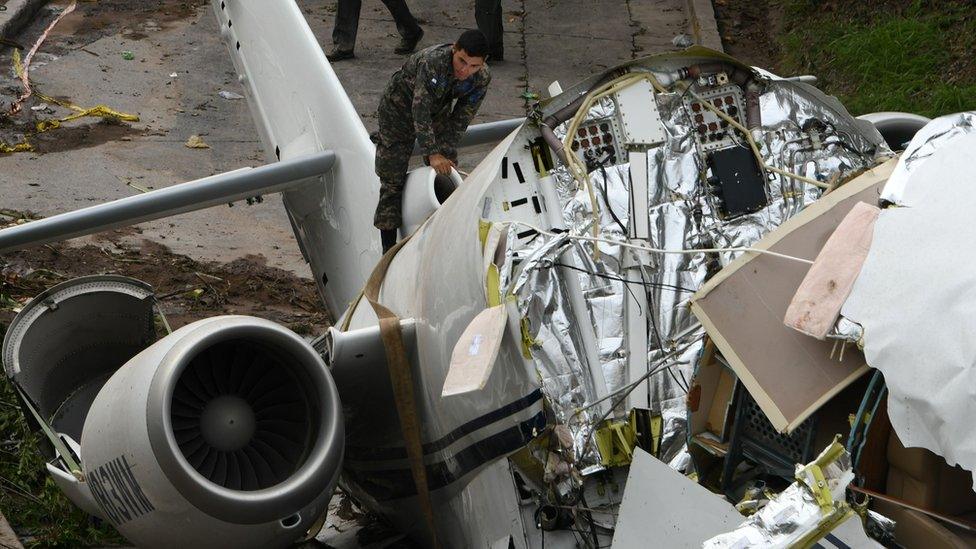 A military person climbs on top of the tail end of the collapsed plane