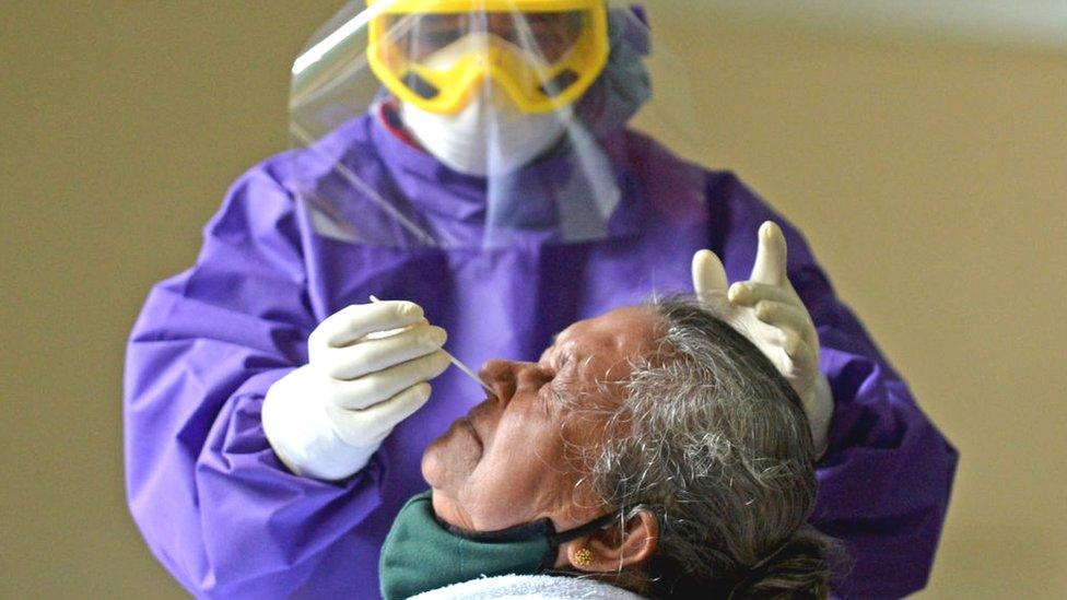 A medical worker wearing Personal Protective Equipment (PPE) gear collects a swab sample