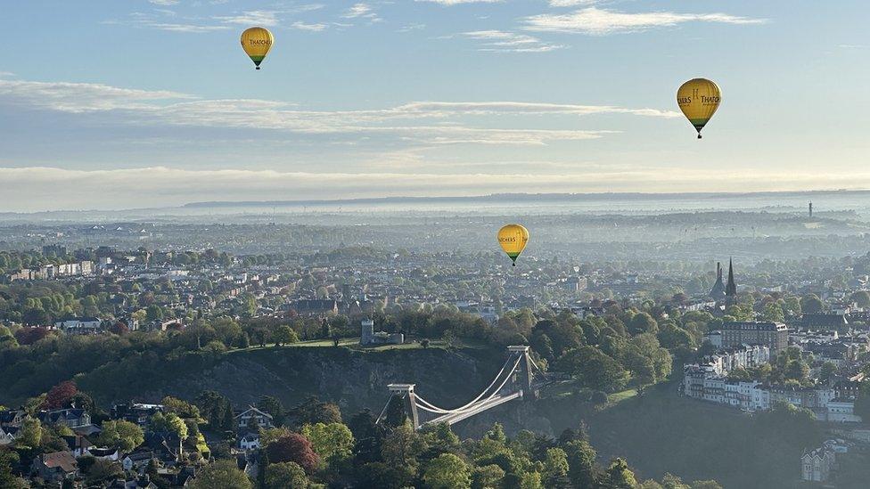 Three hot air balloons over Bristol with the Clifton Suspension Bridge in the foreground on a sunny day