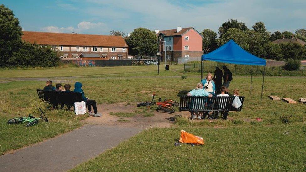 A public grassy patch in Hartcliffe with a small blue tent and people sat around on benches.