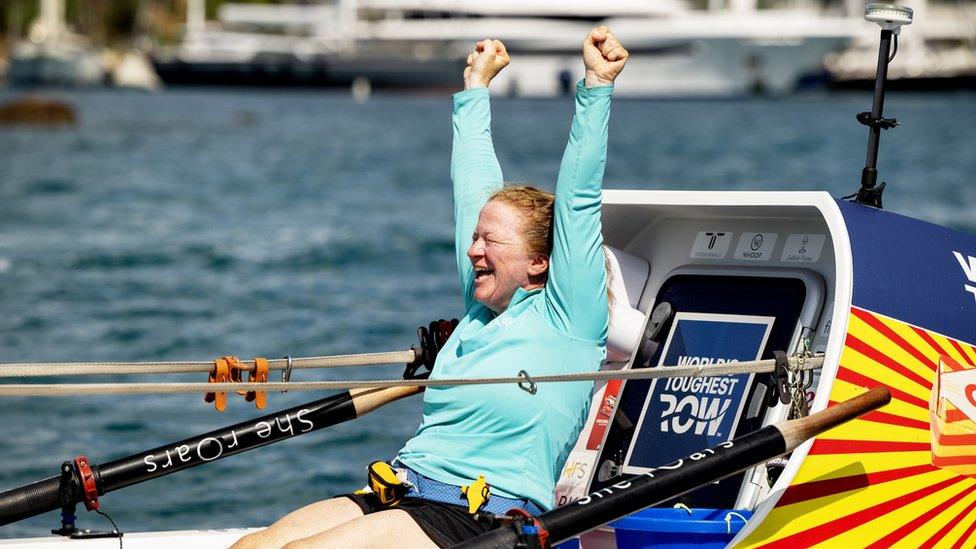 Leanne in her boat raising her arms in celebration