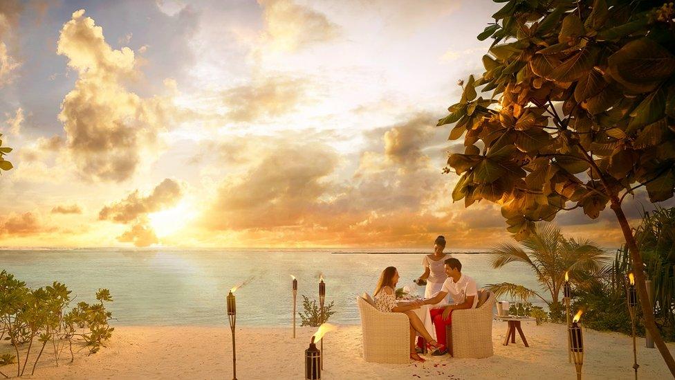 Couple having dinner on sandy beach at sunset