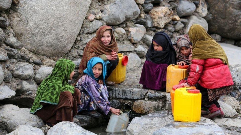 Afghan girls fill drinking water canisters.