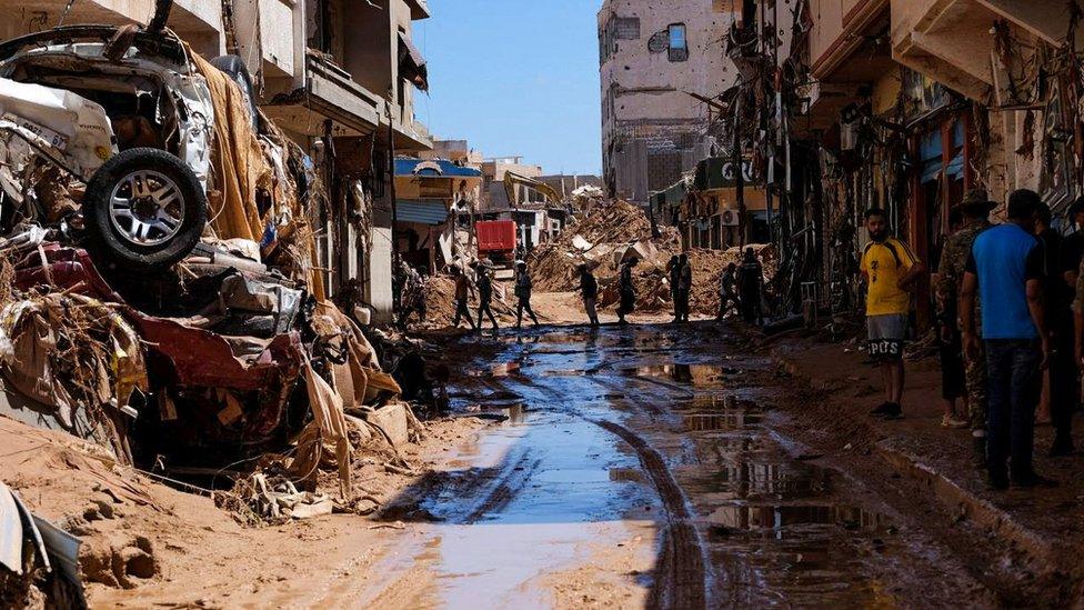 People walk next to damaged houses, following a powerful storm and heavy rainfall hitting the country, in Derna, Libya