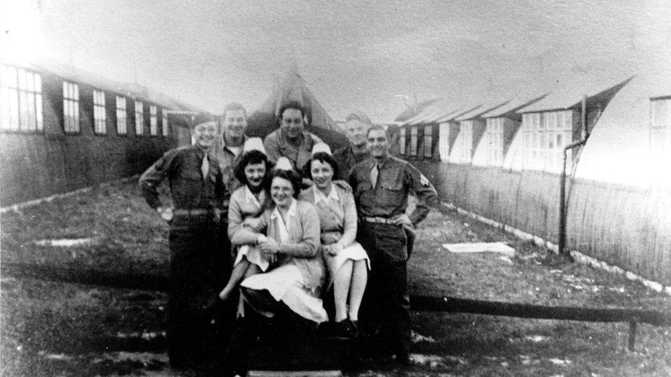 An old black and white picture of soldiers and nurses posing between nissen huts