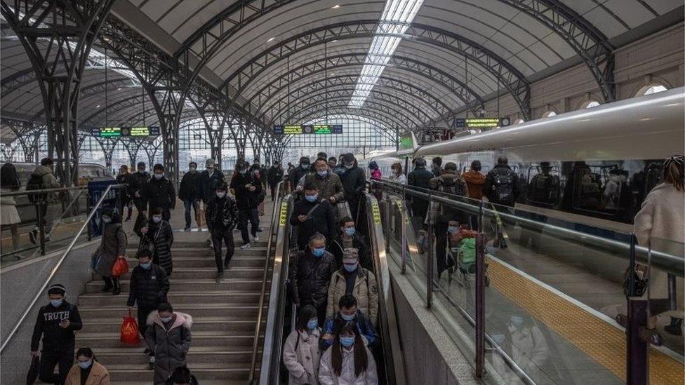 Passengers wearing protective face masks walk with their luggage after arriving to Hankou railway station, in Wuhan, China, 21 January 2021.