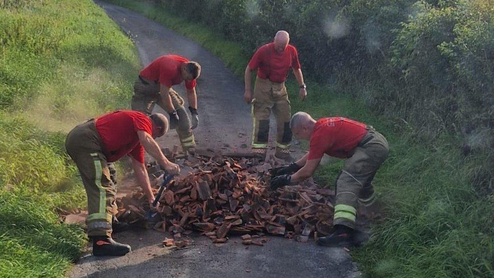 Four firefighters working to clear a large amount of flytipping from a narrow, single track country lane.