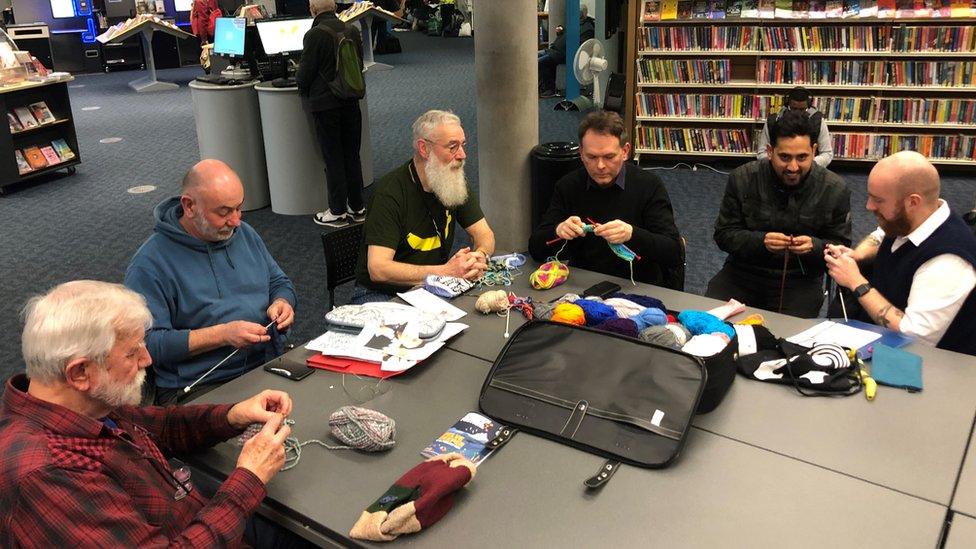 Six men around a table knitting