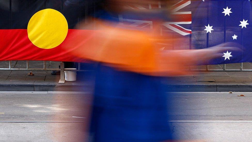 A person walks past the Australian flag and the Aboriginal flag