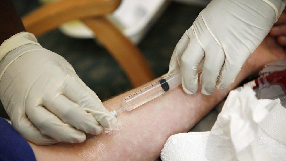 Gloved hand of nurse administering antibiotics into intravenous feed on forearm of patient