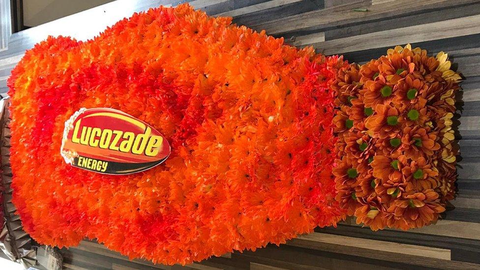 A funeral wreath in the style of a Lucozade bottle