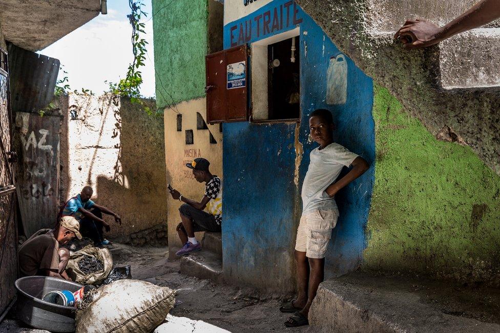 A boy stands and looks at one of the crossroads within the slum. A man on the left is tending to his charcoal shop