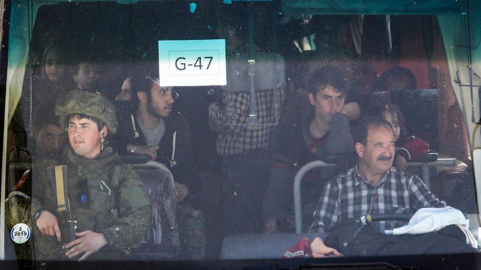 A member of the Russian military police (L) rides in the front of a bus carrying Syrian civilians and rebel fighters evacuated from Eastern Ghouta arriving at a government-held area at the entrance of Harasta on the outskirts of the capital Damascus, on March 25, 2018