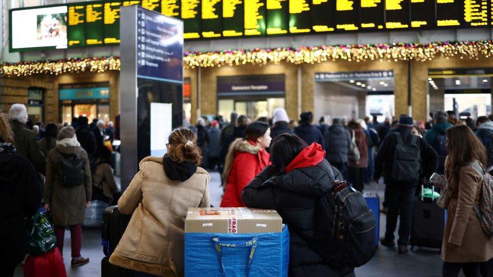 People wait beneath information screens displaying train times at Kings Cross Station in London, after members of the RMT Union working for Network Rail ended their strike on 27 December