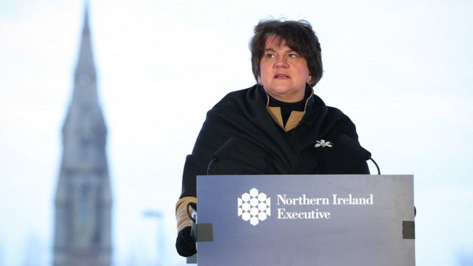 Arlene Foster appearing outside, standing at a podium with NI Executive branding