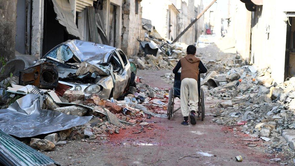 A boy pushes a wheelchair along a damaged street in the east Aleppo neighborhood of al-Mashatiyeh, Syria, in this handout picture provided by UNHCR on January 4, 2017.