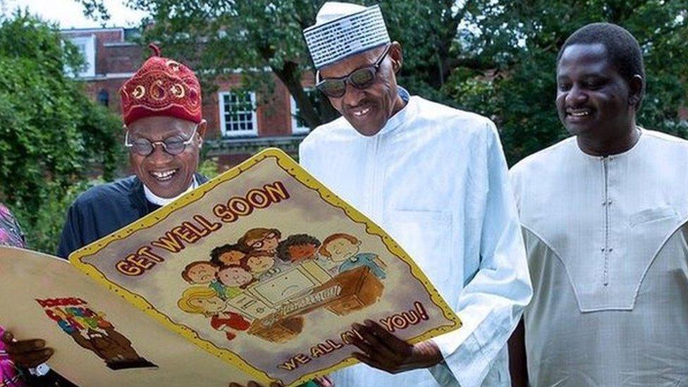 A photograph tweeted by the @NGRPresident account shows President Buhari standing outdoors, grinning and wearing sunglasses while holding a large get well card, with a handful of officials around him.