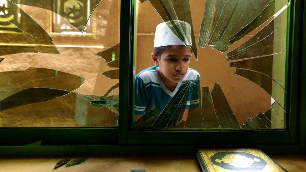 A Muslim boy looks at a smashed mosque window in Sri Lanka, 2018