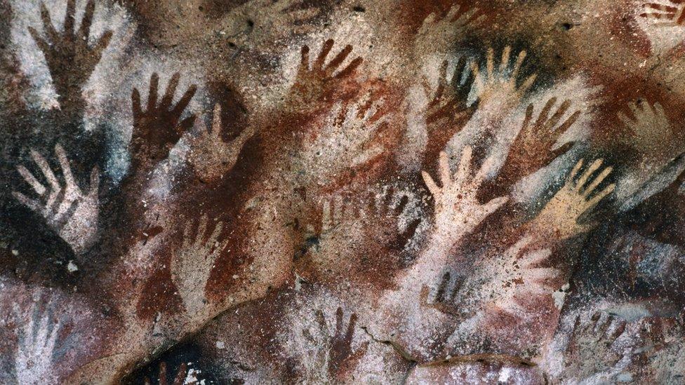 Lots of hands painted onto a cave wall.