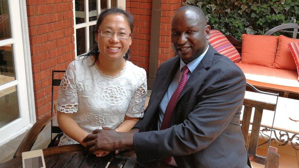 Xu Jing and Henry Rotich hold hands as they sit at a table