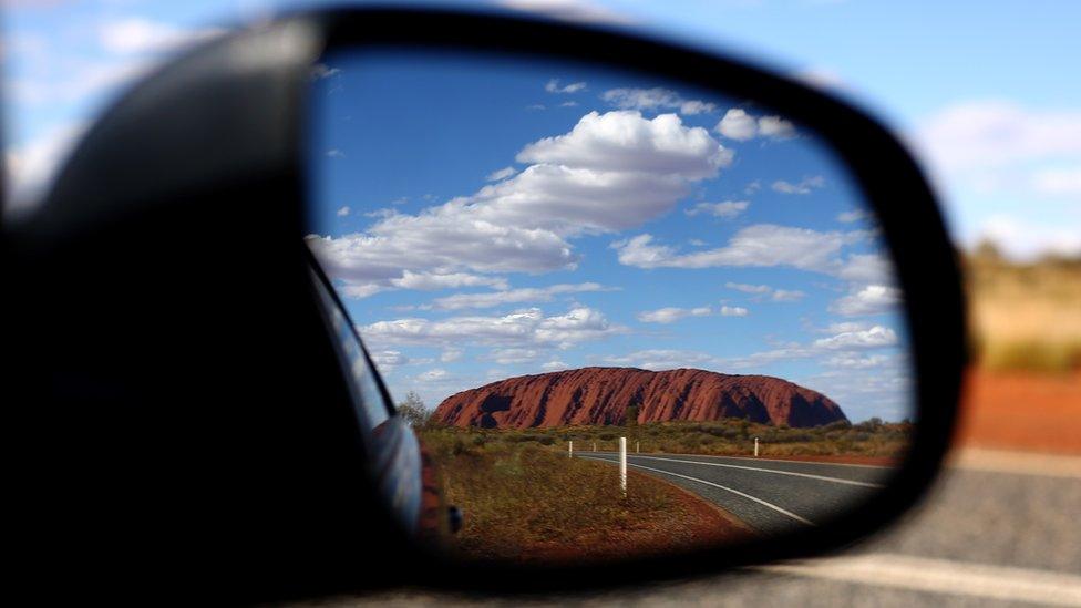 Australia's famed outback landmark, Uluru, pictured in a car's rear view mirror