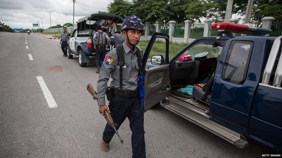 A policeman carries a rifle between waiting trucks outside of the gate of the USDP headquarters in Naypyitaw, Myanmar, 13 August 2015