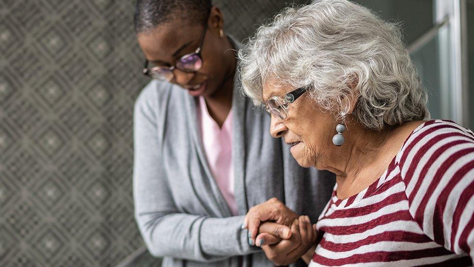 A stock image of an elderly woman being supported by a carer as she walks