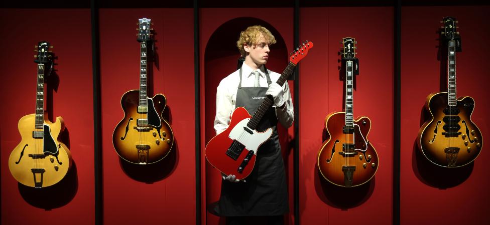 An auction worker holds a Schecter solid body electric guitar during a photo-call for the Mark Knopfler Guitar Collection at Christie's Auction House in London, Britain, 18 January 2024. More than 120 guitars and amps owned by British musician Mark Knopfler will be auctioned on 31 January 2024.