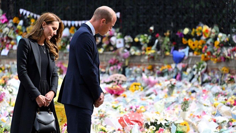 The Prince and Princess of Wales look sombre as they look at flowers left for the Queen