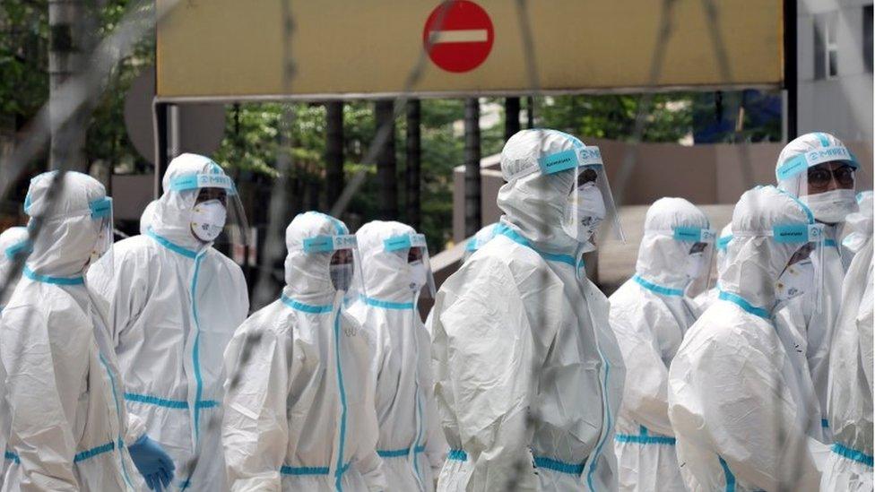 Police officers wearing protective suits gather outside an apartment under enhanced lockdown to pick up illegal immigrants in Kuala Lumpur (1 May 2020)