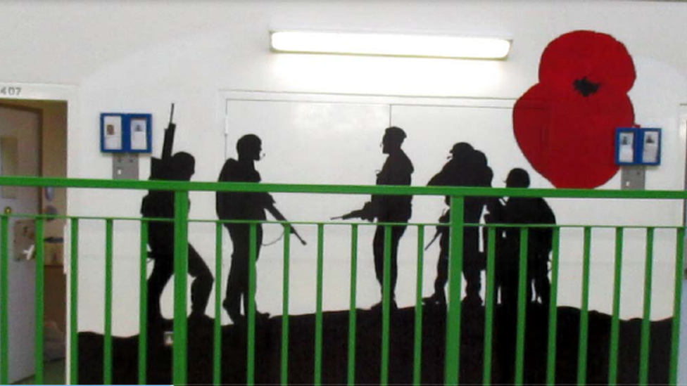 A mural on an interior prison wall of the silhouettes of soldiers and a red poppy