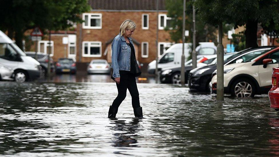 A woman in wellies walks through floodwaters in a carpark near houses in Battersea, London