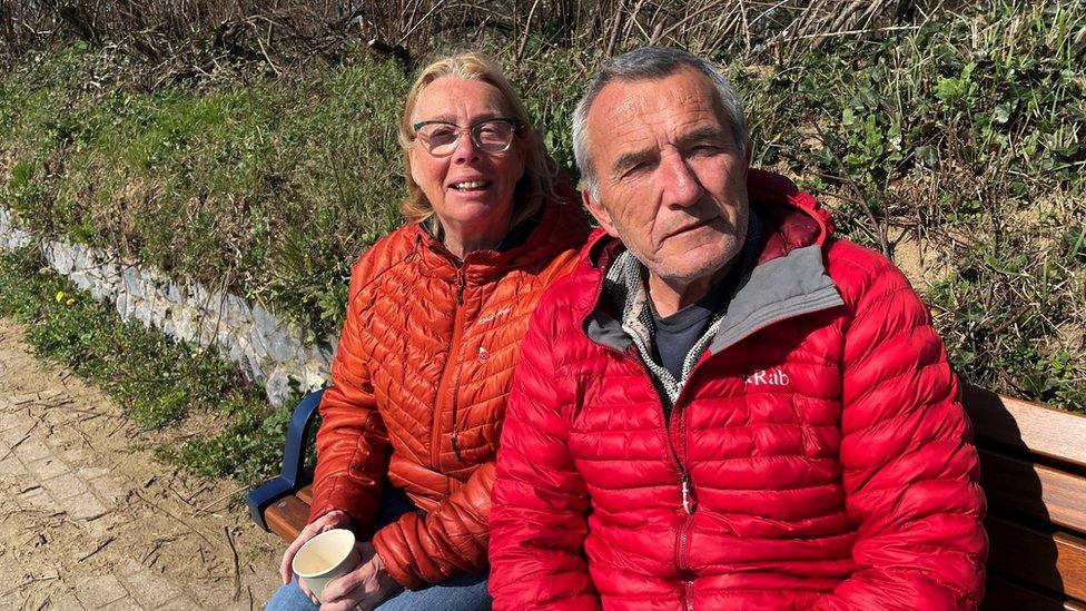 Martyn and Caroline Bagley sitting on a bench by the beach