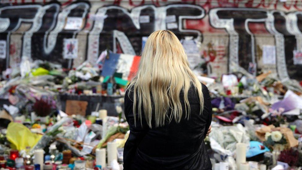 A woman stands in front of a makeshift memorial