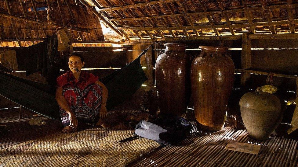 A woman from the Bunong indigenous group sits beside jars of rice wine in her home on August 8, 2014 in Mondulkiri, Cambodia